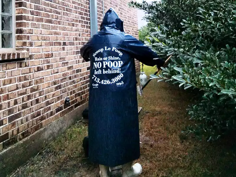 Scoop le Poop waste specialist working in the rain Scoop le Poop waste specialist working in the rain in a branded, dark blue rain slicker that says "Rain or Shine, no poop left behind" on the back.